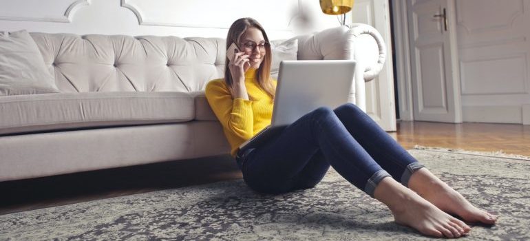 A woman in a yellow shirt sitting on a floor with a laptop,