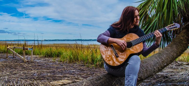 A woman sitting on a tree in nature and playing a classical guitar