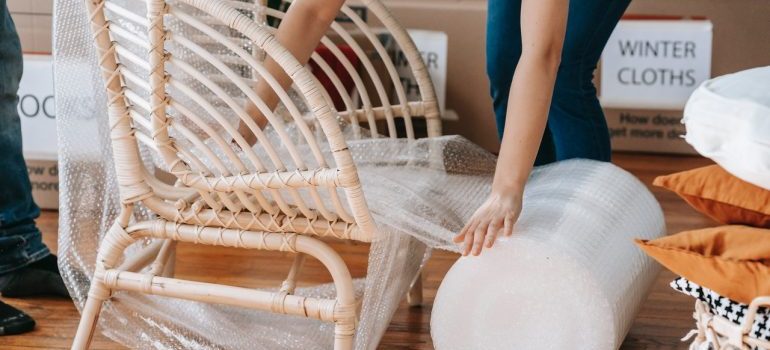 Person wrapping a wooden armchair in bubble wrap.